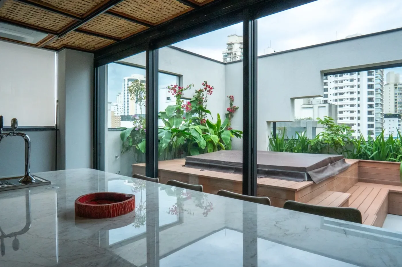 Terraço de apartamento com deck, ofurô e maciço de vegetação nativa, com prédios de São Paulo ao fundo