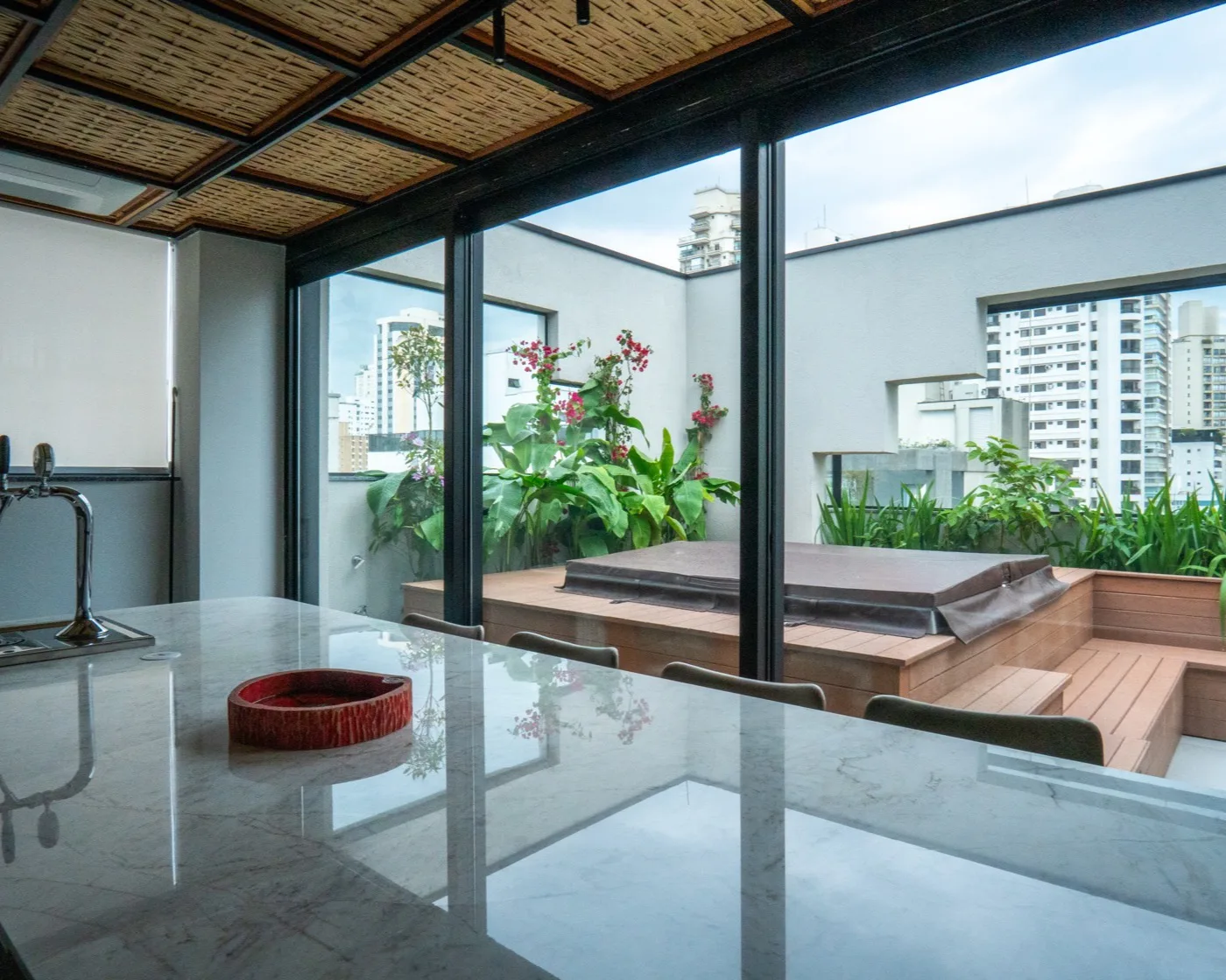 Bancada da churrasqueira aberta para o deck, com bougainvillea e manacá-da-serra florindo no terraço