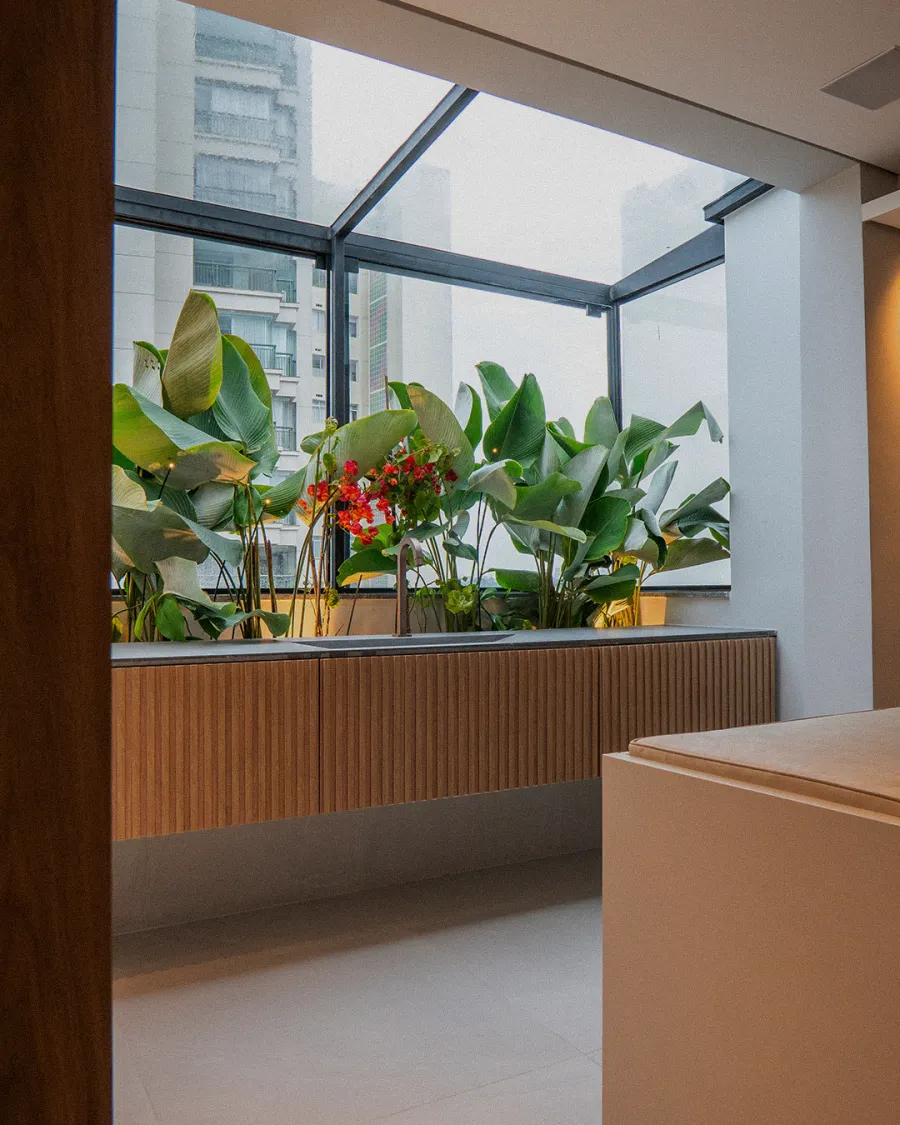 Jardim de inverno envidraçado com folhagens tropicais e buganvília vermelha, visto de dentro do apartamento